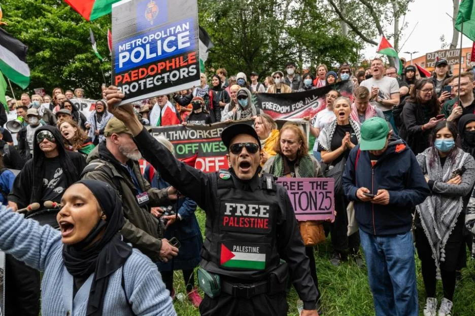 Pro-Palestine protesters holding signs, including one that reads "Metropolitan Police Paedophile Protectors," at a rally.
