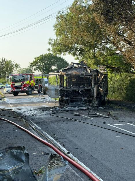 A fire engine completely burned out on a road next to another, undamaged fire engine.
