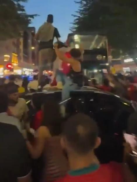 Egyptian fans celebrating on a street at night, with some standing on a car and others waving flags.