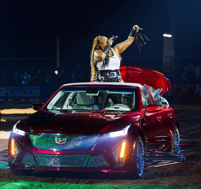 Lizzo performing from the roof of a red Cadillac convertible.