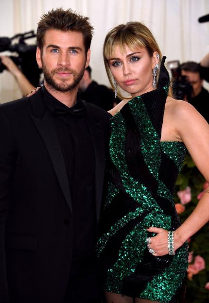 Liam Hemsworth and Miley Cyrus, dressed in formal attire, posing for a photo.