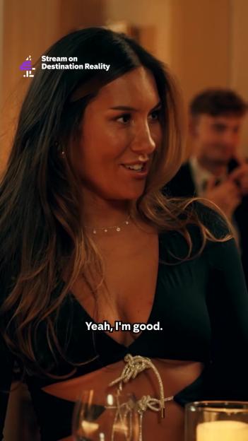 A woman in a black top with cutouts around the waist and a man in the background.