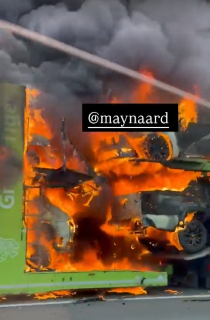 A multi-level car carrier truck engulfed in flames with several cars on fire.