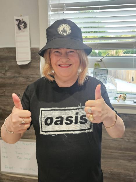 A woman in a black bucket hat and black Oasis t-shirt giving a double thumbs-up.