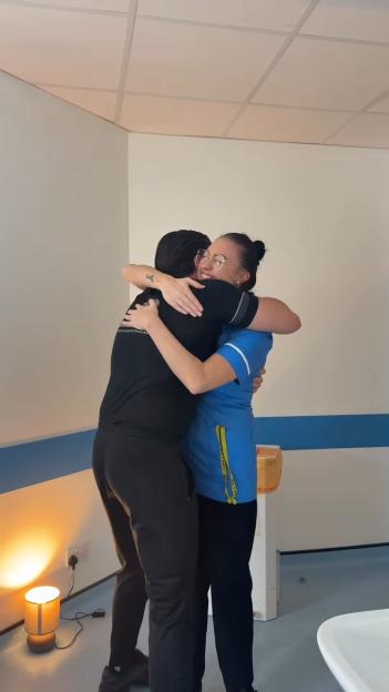 A person in a black shirt embracing a nurse in a blue uniform, smiling.