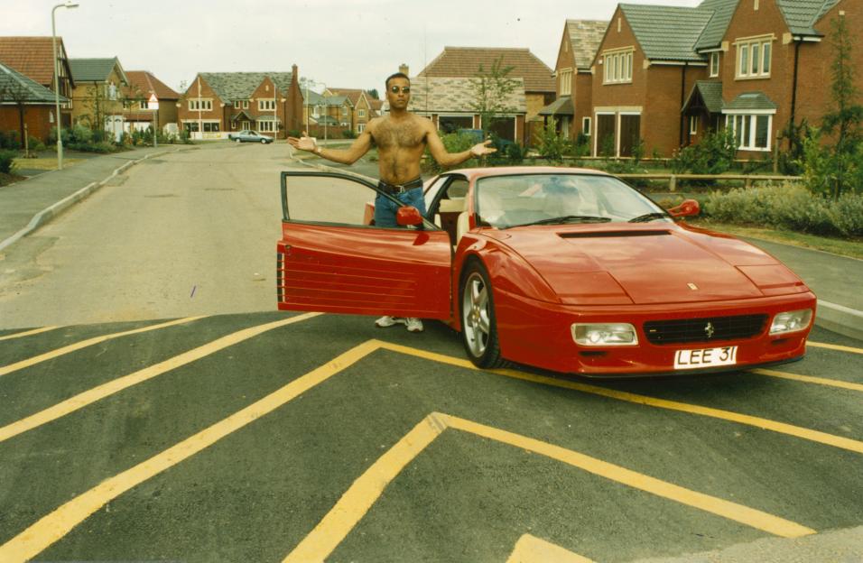 National Lottery winner Lee Ryan standing next to his red sports car.