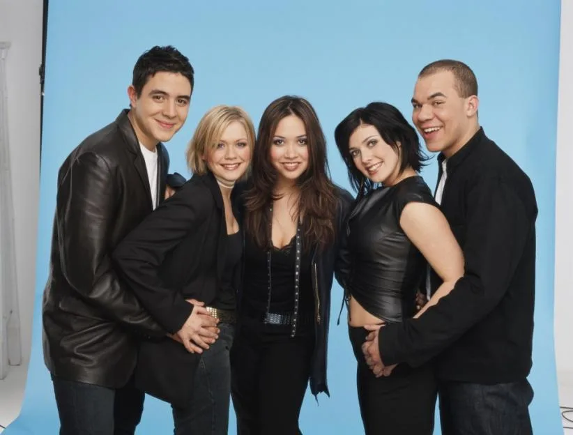 British pop group Hear'Say posing together in a studio against a blue background.