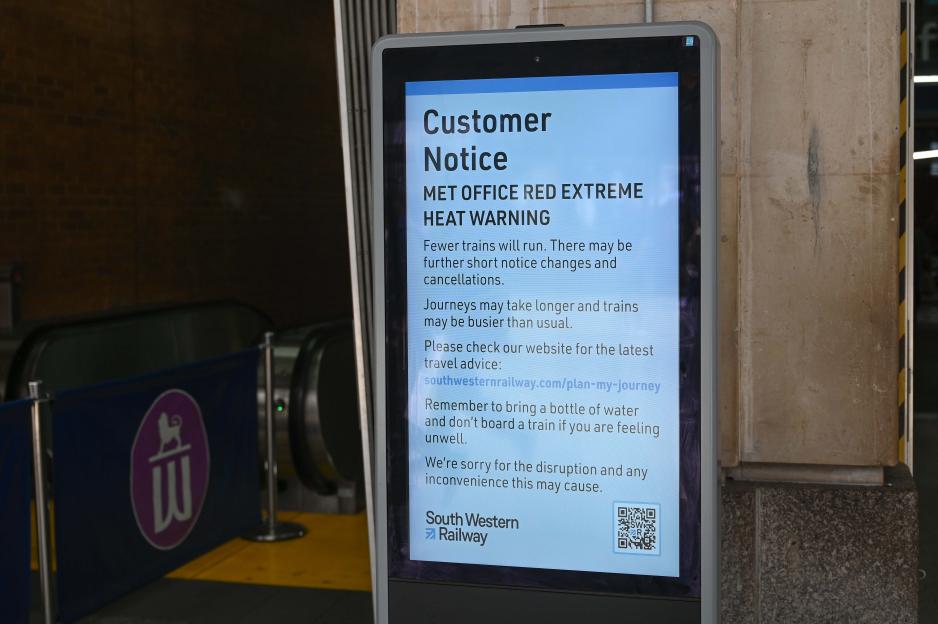A digital sign at South Western Railway station in London displaying a "MET OFFICE RED EXTREME HEAT WARNING" notice.
