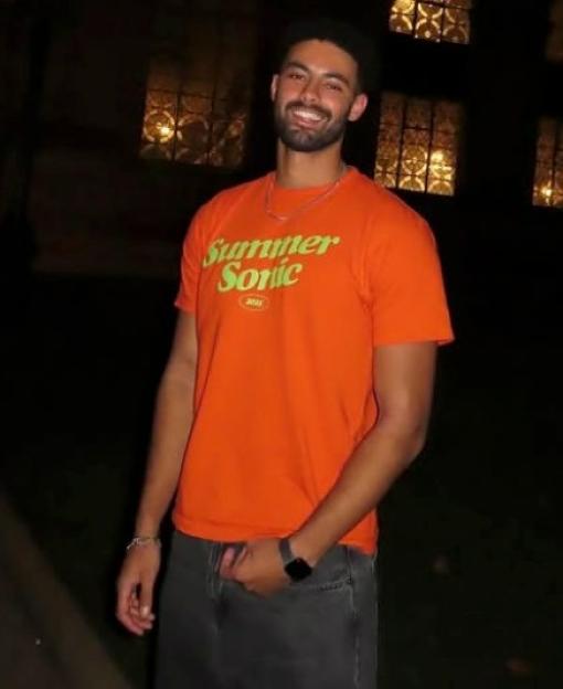 Luca Smith, brother of pop star Jorja Smith, smiling in a dark setting with buildings and a streetlamp in the background.