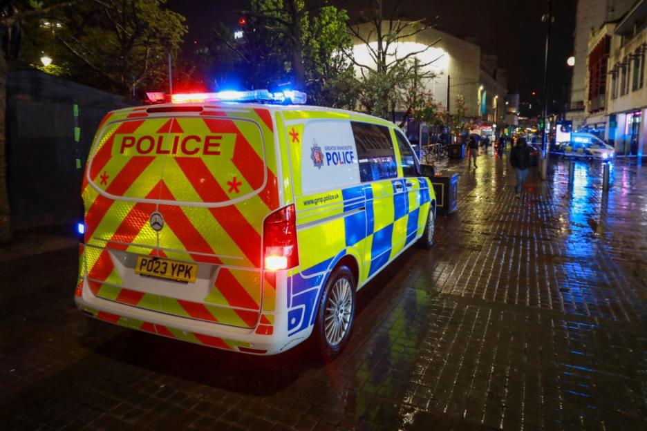 Police van with flashing lights on a wet street at night in Manchester City Centre.