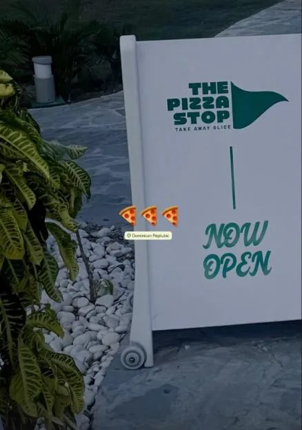 A white sign for "The Pizza Stop" that says "NOW OPEN" in green text, with three pizza emojis and a location tag for "Dominican Republic".