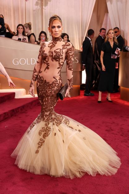 Jennifer Lopez on the red carpet at the Golden Globes, wearing a sheer, long-sleeved, high-neck brown gown with a voluminous cream tulle skirt.