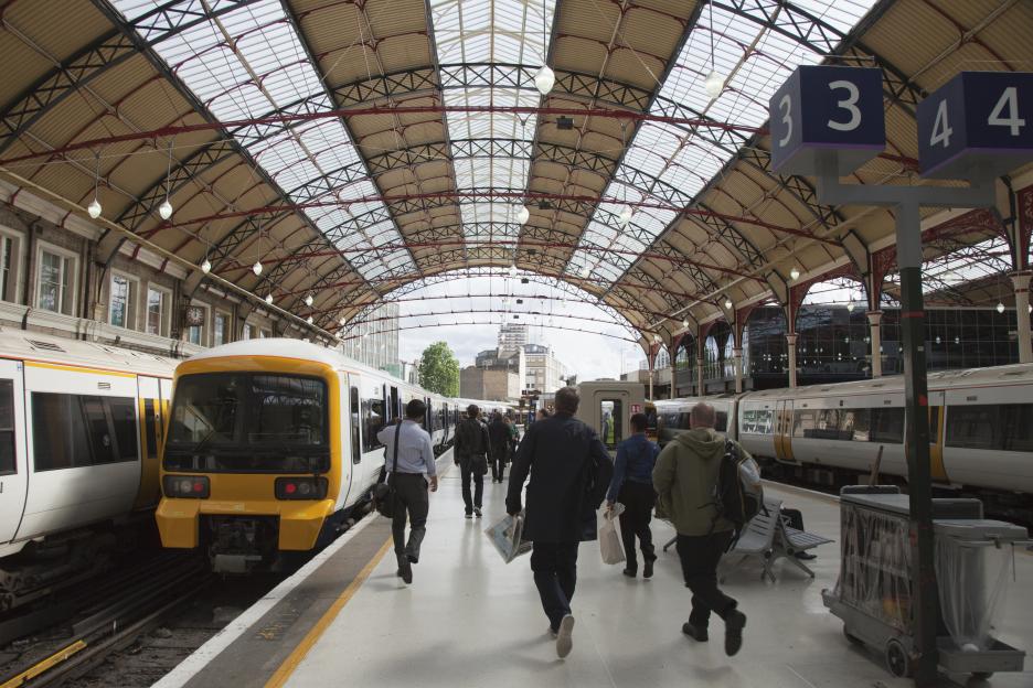 People walking and running on a platform in Victoria Station, with trains on either side under a high, arched roof.