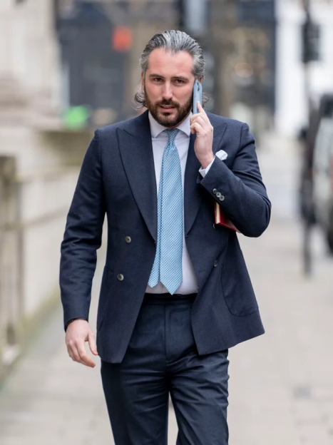 Man in a navy suit and light blue tie talking on a cell phone while walking.