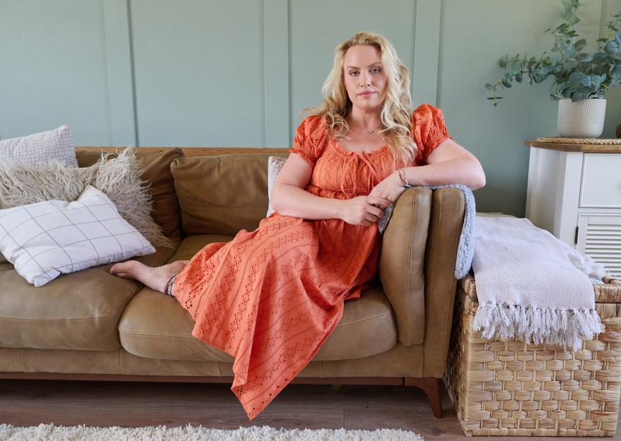 Woman with blonde hair sitting on a brown couch in an orange dress.