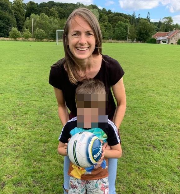A smiling woman with long brown hair, Elisabeth-Jane Ross, with her child in a field holding a soccer ball.