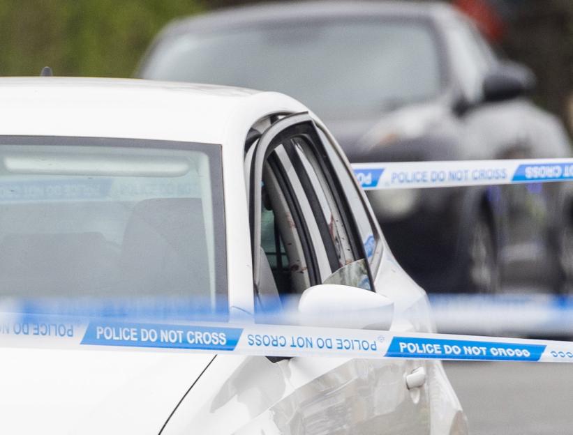 Police tape with "POLICE DO NOT CROSS" wrapped around a white car.