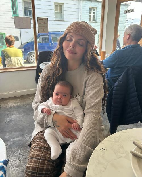 Jesy Nelson holding a baby on her lap in a restaurant.