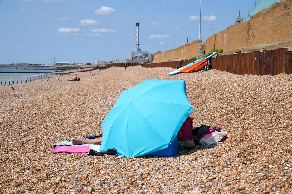 Person relaxing under a beach umbrella on a pebble beach.
