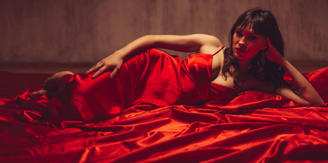 Young woman in a red dress lying on red bed sheets.
