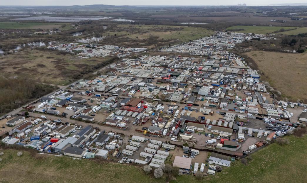 Aerial view of Buckles Lane traveler site in South Ockendon, Essex, featuring numerous trailers and temporary structures amidst a rural landscape.