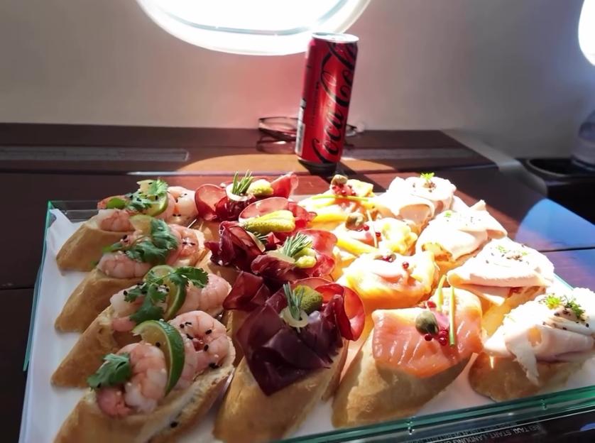 An assortment of canapés including shrimp, cured meats, and smoked salmon on baguettes, served with a Coca-Cola can.
