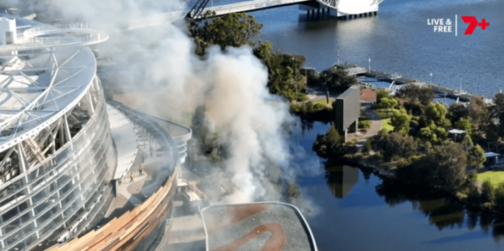 Smoke rises from a fire near a building and a body of water.
