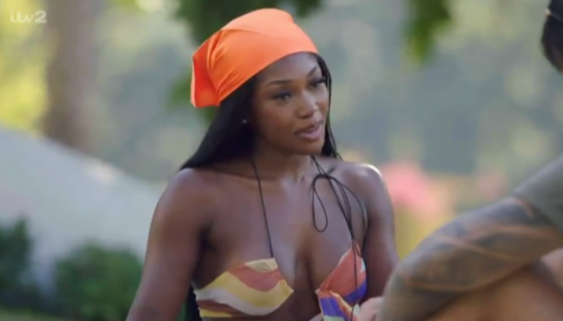 A woman in an orange bandana and colorful bikini top speaking to someone off-camera.