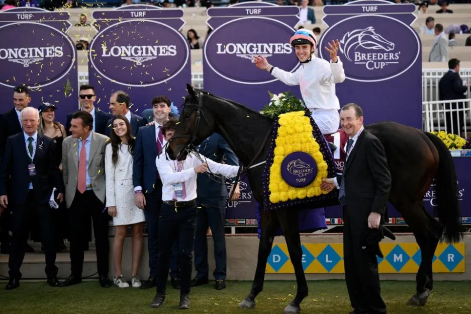 Jockey Dylan McMonagle waves in celebration aboard Ethical Diamond after winning the Breeders' Cup Turf race, surrounded by team members and confetti.