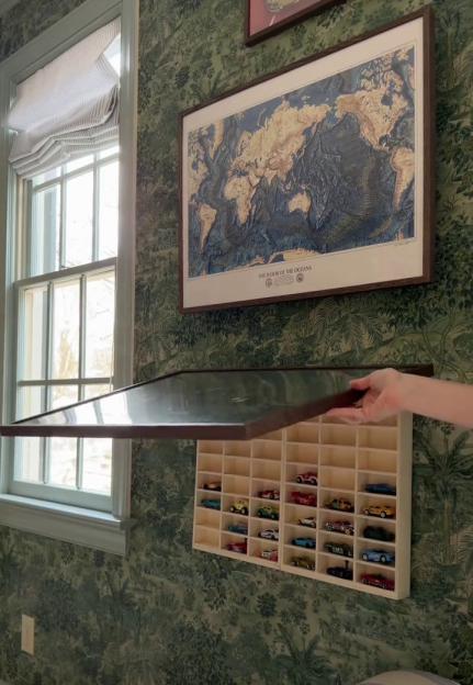 A hand opening a framed world map to reveal a hidden compartment filled with toy cars.