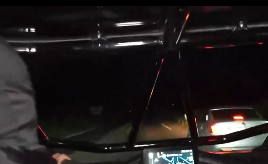 View from a car's interior at night, showing the dark road ahead and the taillights of a car in front.
