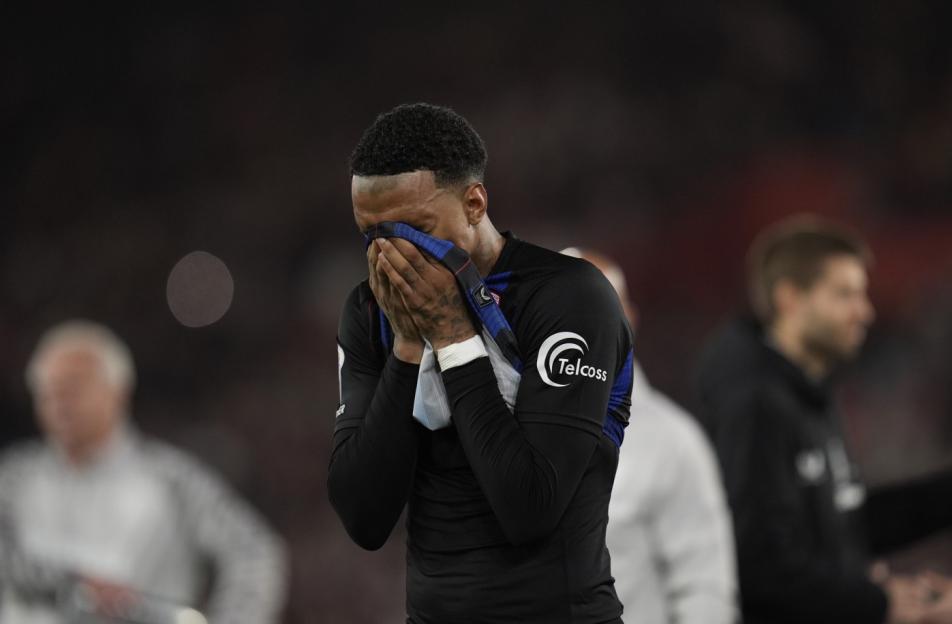 A Southampton player with curly dark hair holds a blue and white cloth to his face, looking distressed.