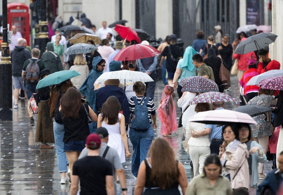 Crowd of people in Trafalgar Square, London, walking with umbrellas during a rain shower after a long summer drought.