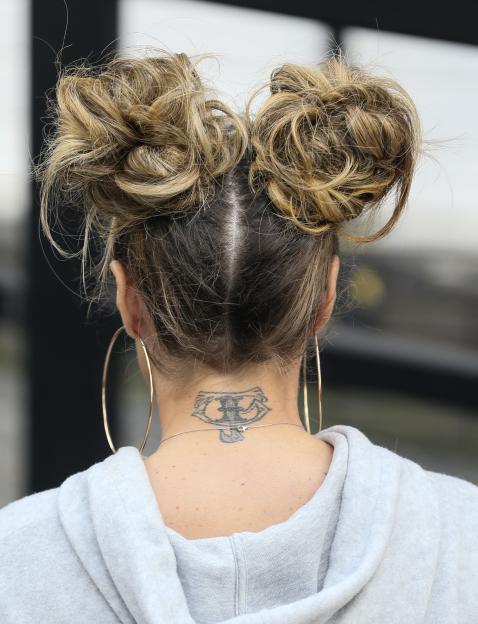 The back of Katie Price's head showing two messy buns, hoop earrings, and a neck tattoo.
