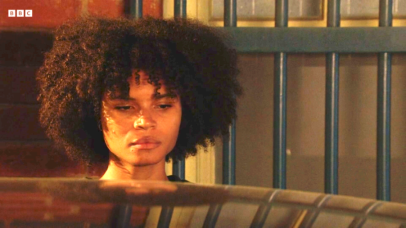 A close-up of a woman with curly hair looking down, with a BBC logo in the top left corner.