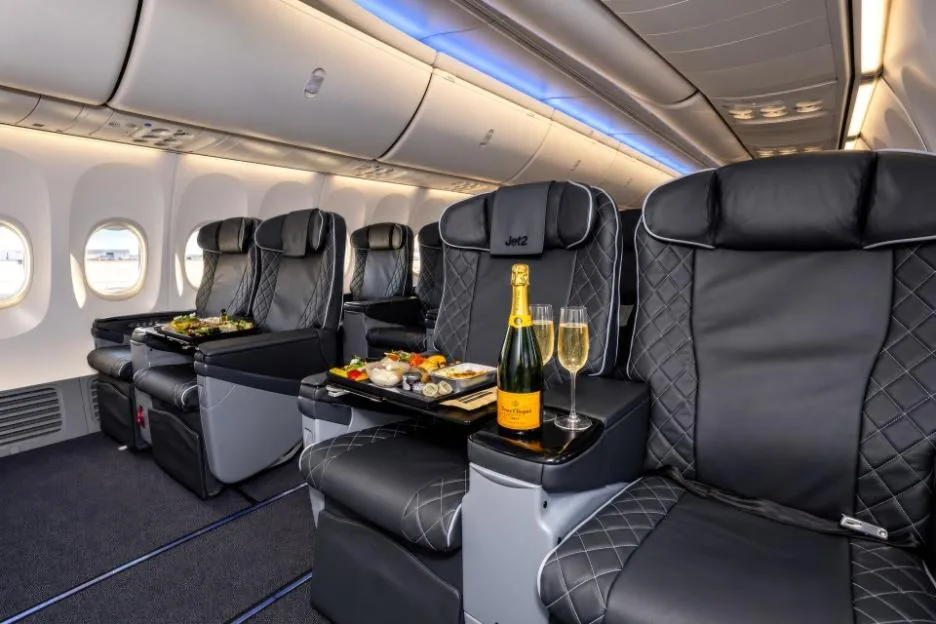 Interior of Jet2's new VIP configured aircraft, showing rows of black leather business class seats with a bottle of champagne and food on a tray table.