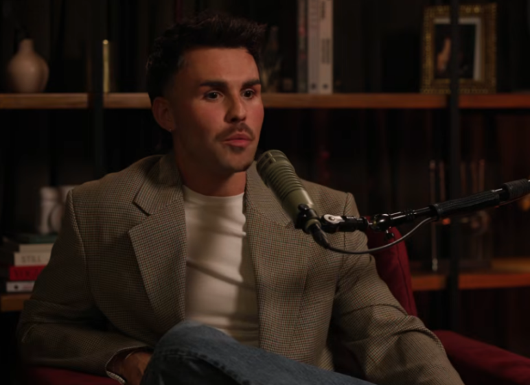 A man wearing a blazer and white shirt speaks into a microphone.