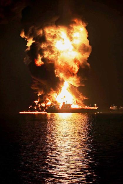 Oil tanker on fire at night with flames and smoke billowing into the sky.