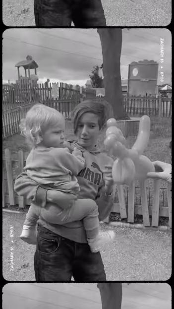 A black and white photo of a boy holding a toddler and a balloon animal.