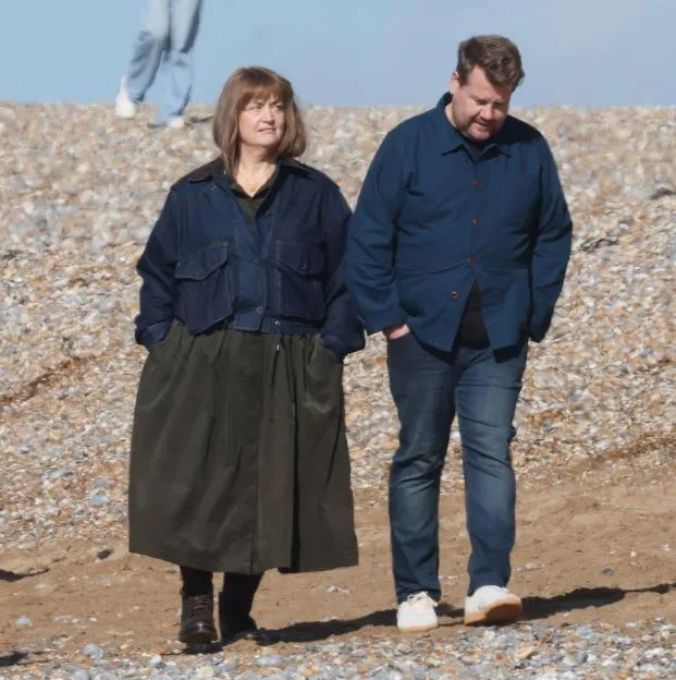 James Corden and Ruth Jones walk along a pebbled beach during the filming of the Apple TV series The Choir.