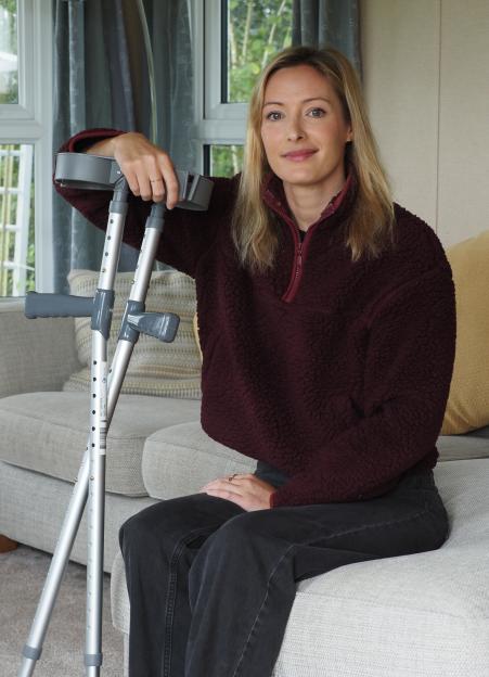 Holly Wiffen, an adrenaline junkie, sits on a couch with crutches after sustaining injuries from a skydiving accident.