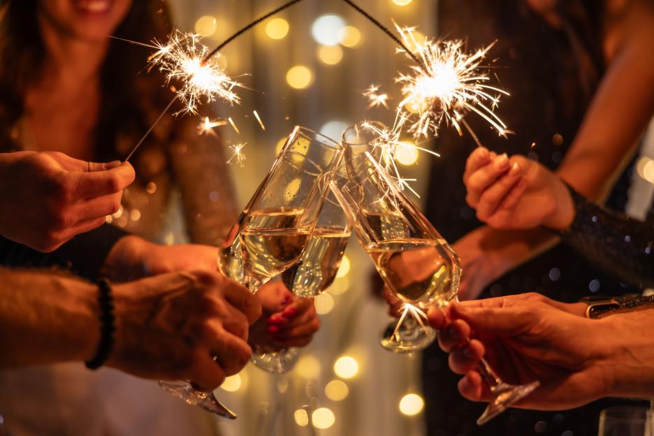 Hands holding sparkling sparklers and champagne flutes making a toast.