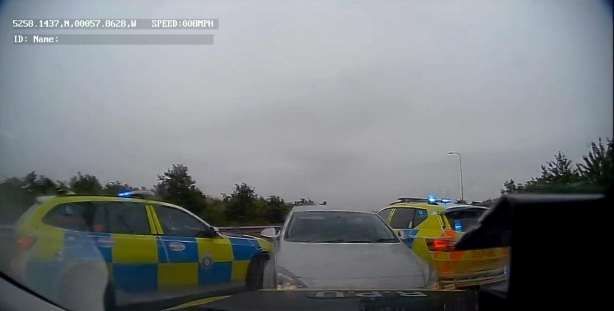 Police vehicles boxing in a silver car on a highway.