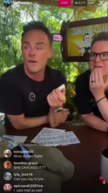 Two men on a live broadcast, one holding a small white object, the other covering his mouth.