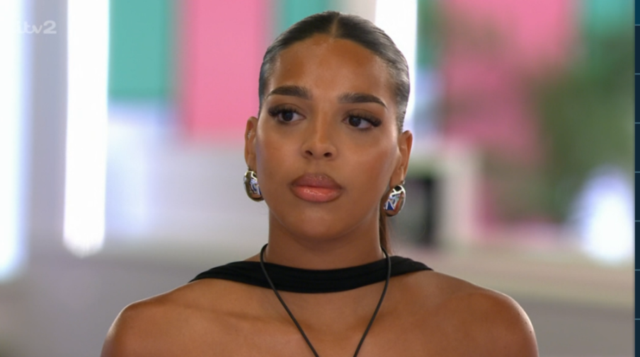 A woman with dark hair pulled back, wearing a black top and silver earrings, looks to her left.
