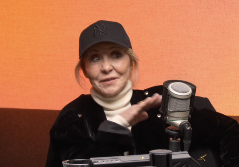 Lulu wearing a Yankees cap and white turtleneck during a podcast interview.