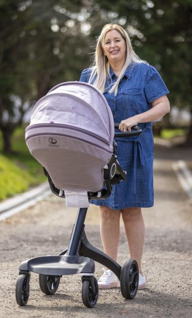 A woman in a denim dress stands outside with a baby stroller.