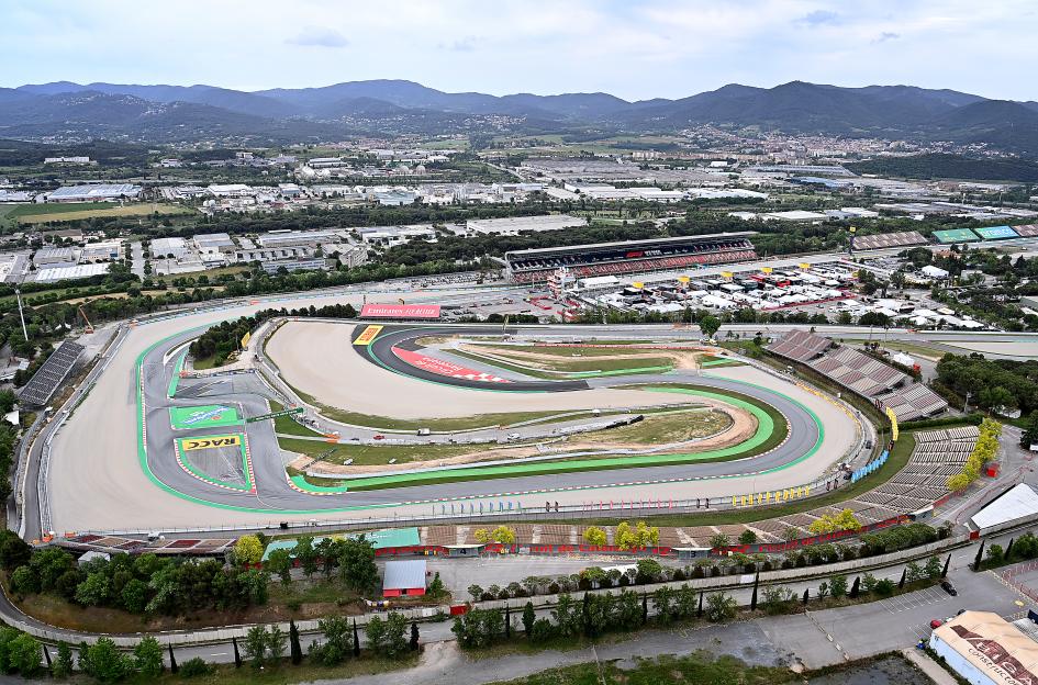 An aerial view of the Circuit de Barcelona-Catalunya F1 racetrack with grandstands and mountains in the background.