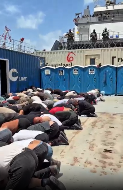 Activists lie on the ground with Israeli soldiers standing guard on a ship above.