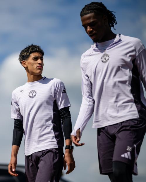Two Manchester United players in training gear walk outdoors.